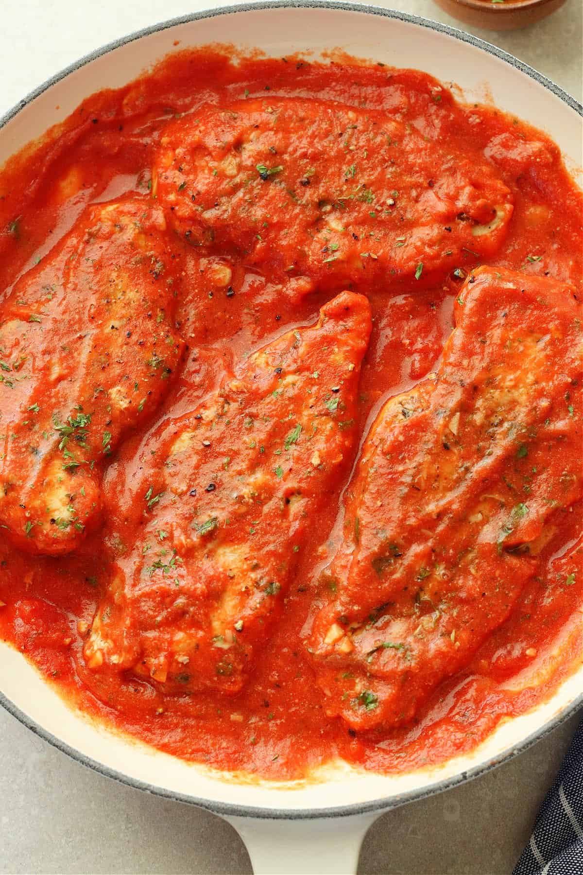 Overhead image of four chicken breasts in a tomato sauce in a skillet.