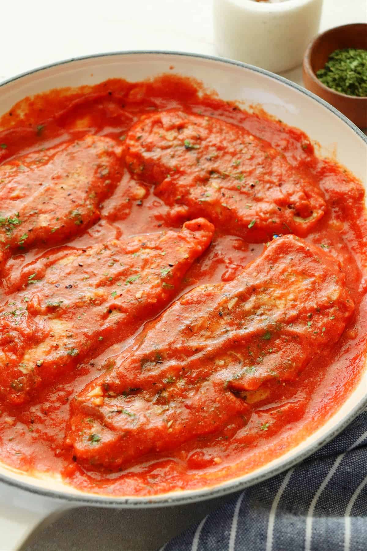 Chicken and tomato sauce in a skillet with a kitchen towel next to it.