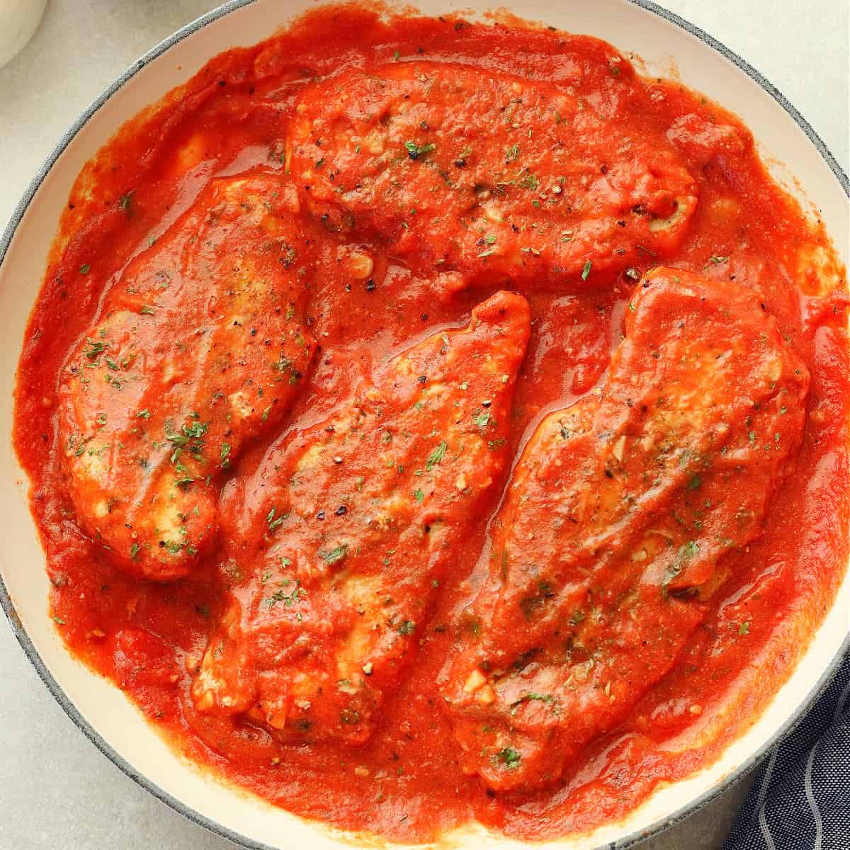 Square image of chicken breasts in a creamy tomato sauce in a skillet.