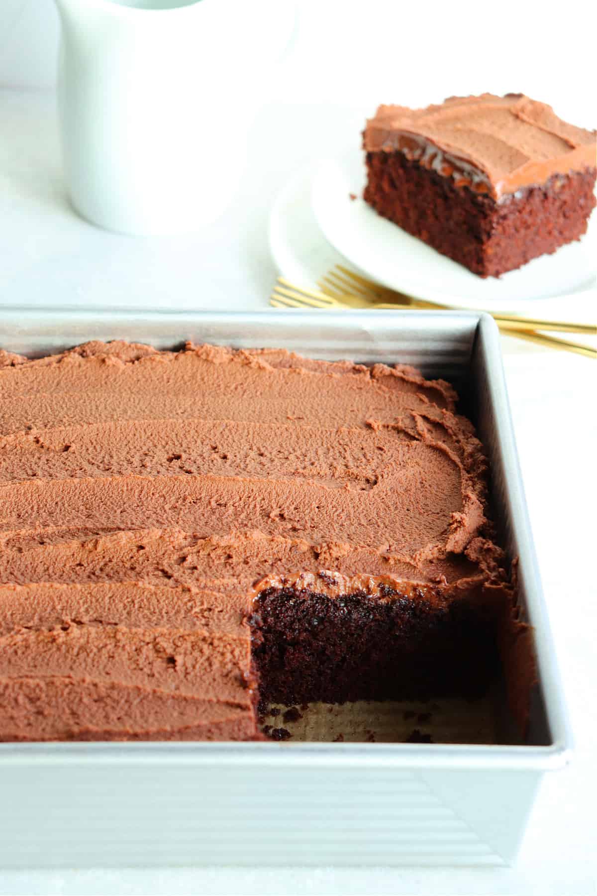 Frosted chocolate cake in a square baking pan with one piece cut out.