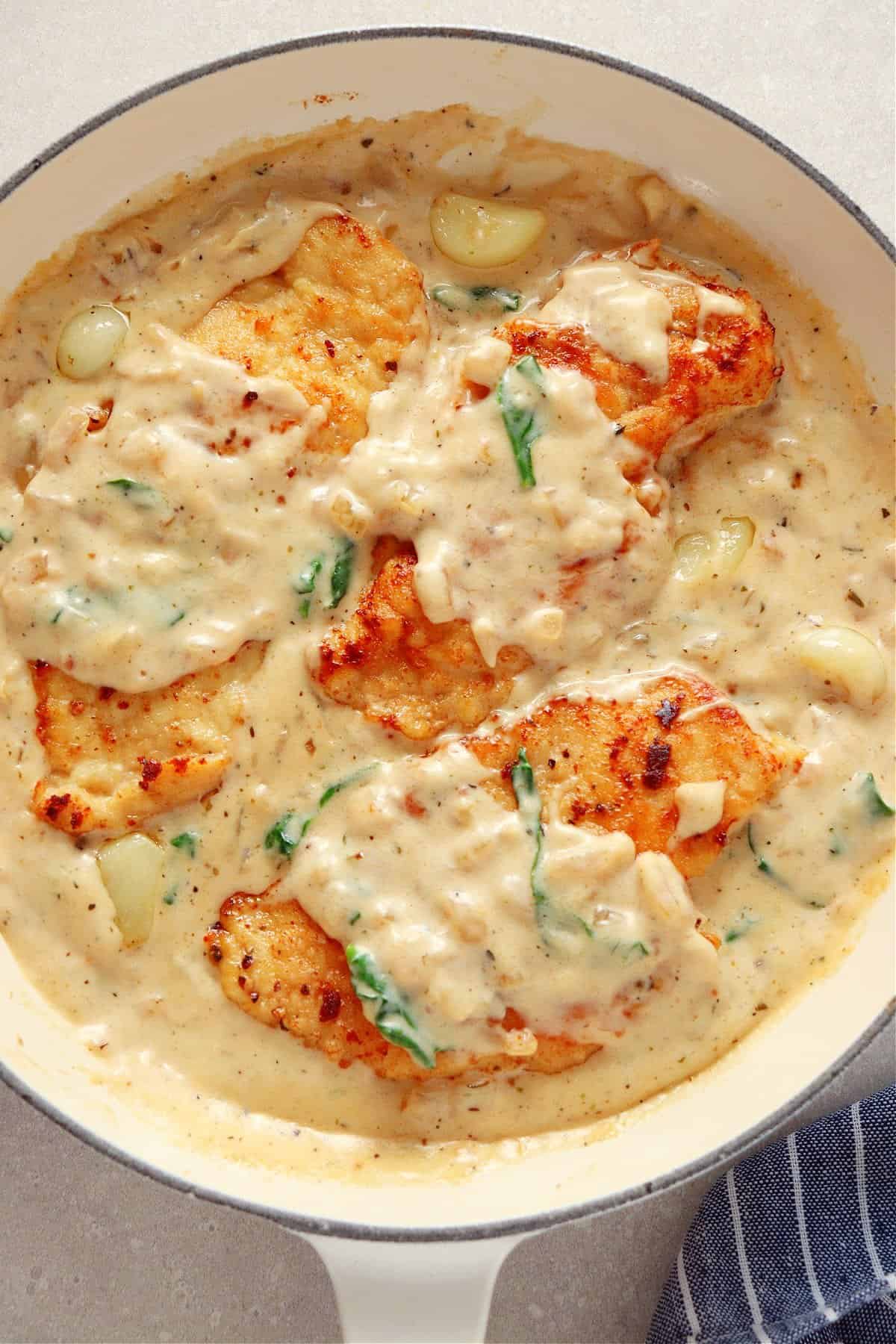 Chicken in creamy sauce in a white enameled cast iron pan, on a gray board.