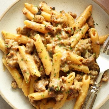 Penne with sausage and creamy sauce on a gray plate with fork.