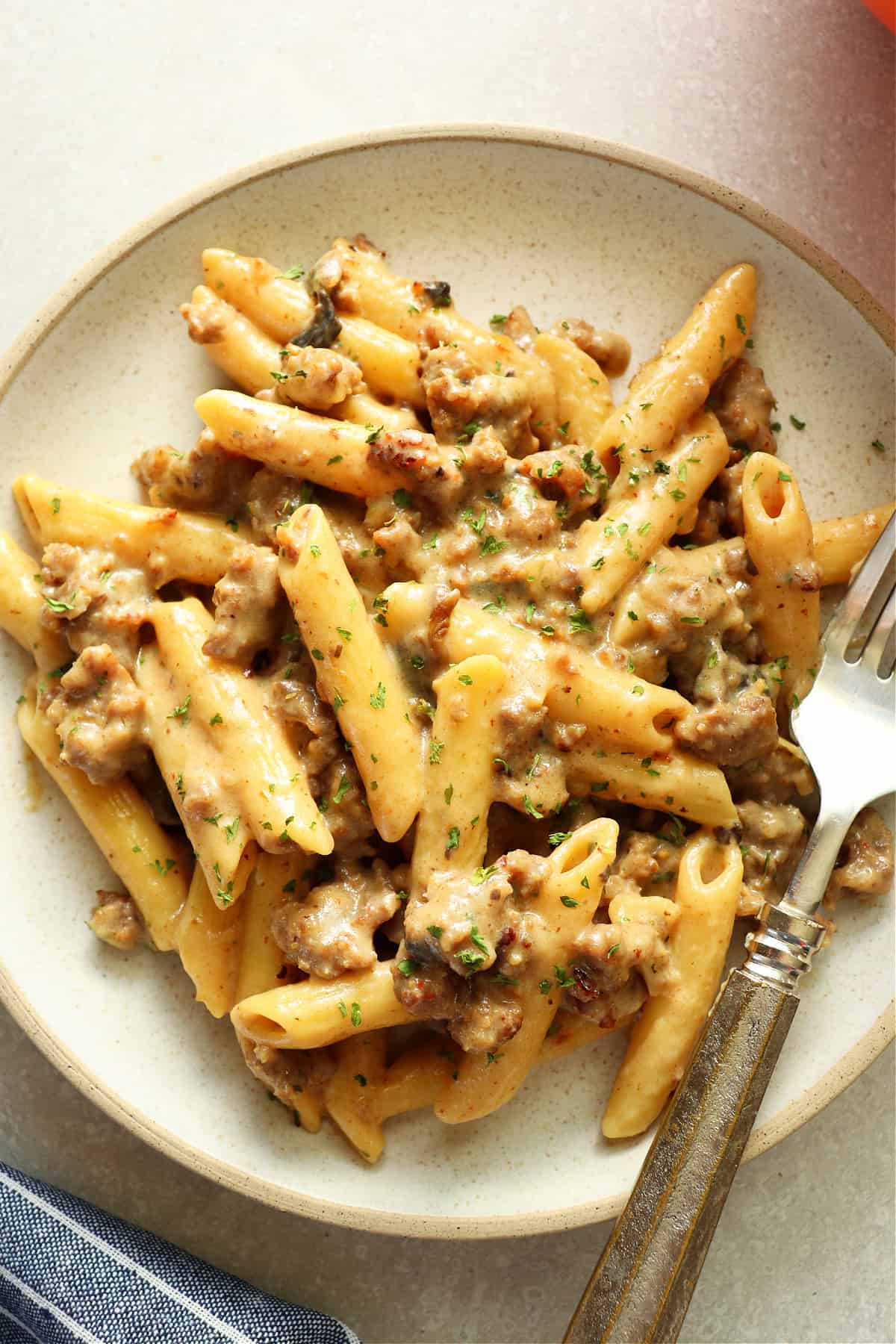 Penne with sausage and creamy sauce on a gray plate with fork.