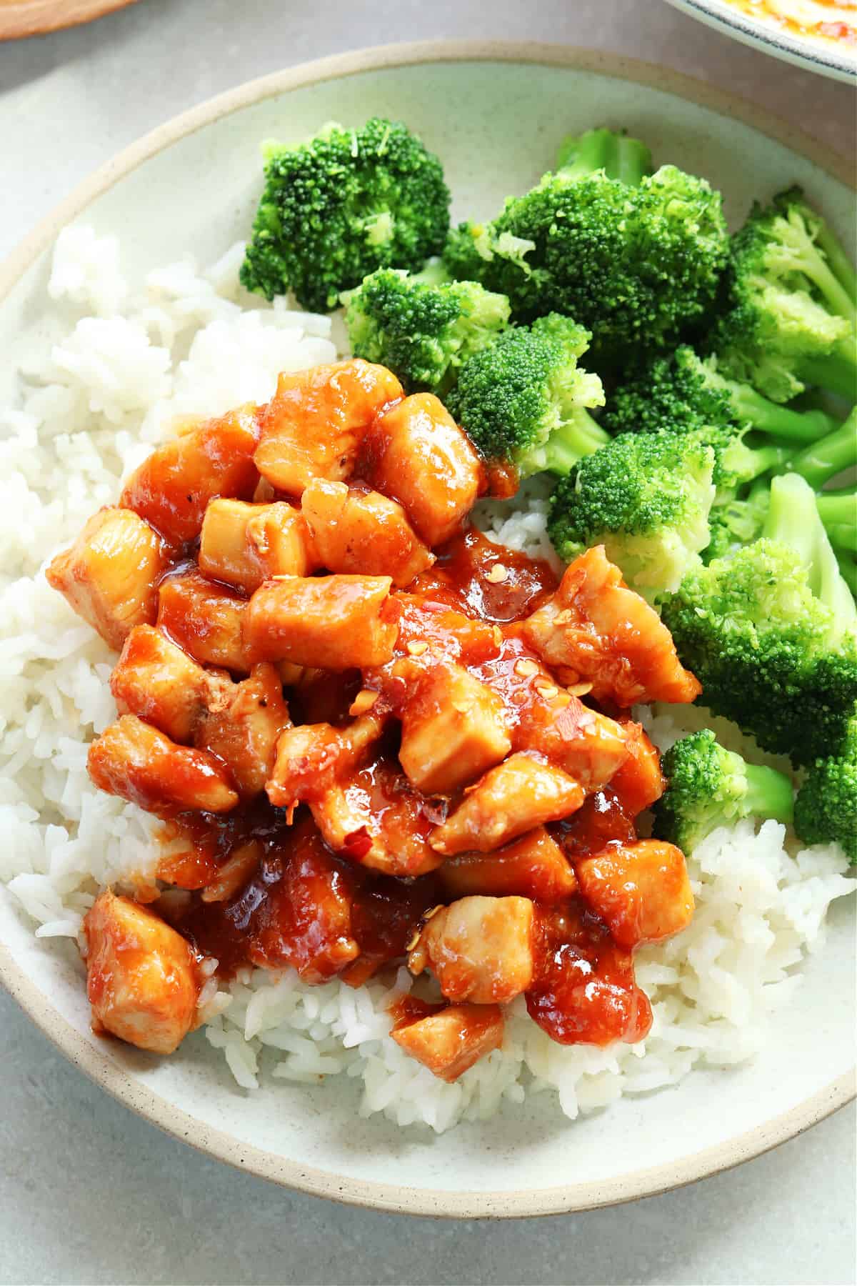 Chunks of chicken in ginger sauce on a bed of rice and broccoli, on a gray plate.