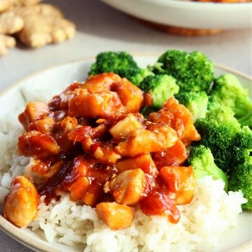 Ginger soy chicken on top of rice with broccoli on the side, on a plate.