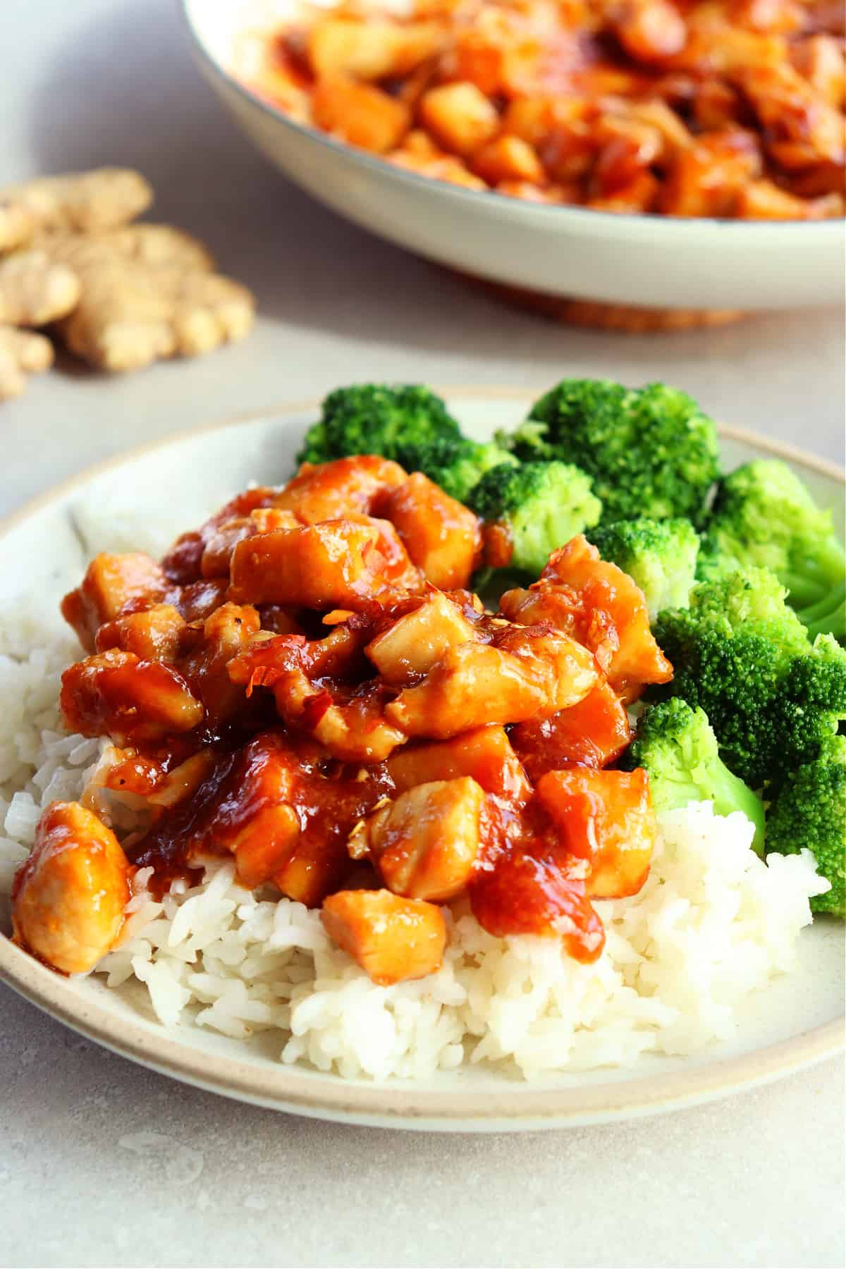 Ginger soy chicken on top of rice with broccoli on the side, on a plate.