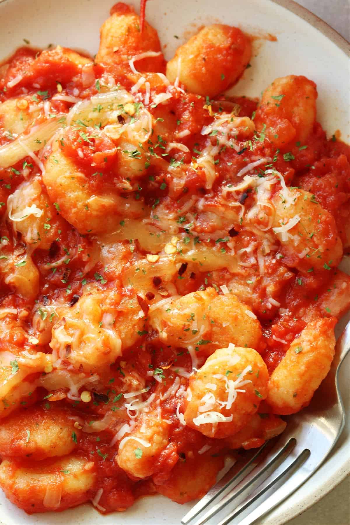 Gnocchi in tomato sauce with Parmesan on a cream plate.