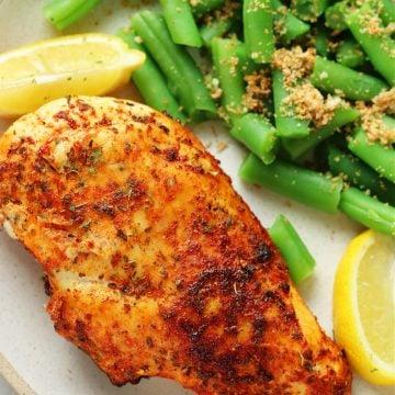 Air fried chicken breast with lemon wedges and green beans on a dinner plate with fork.