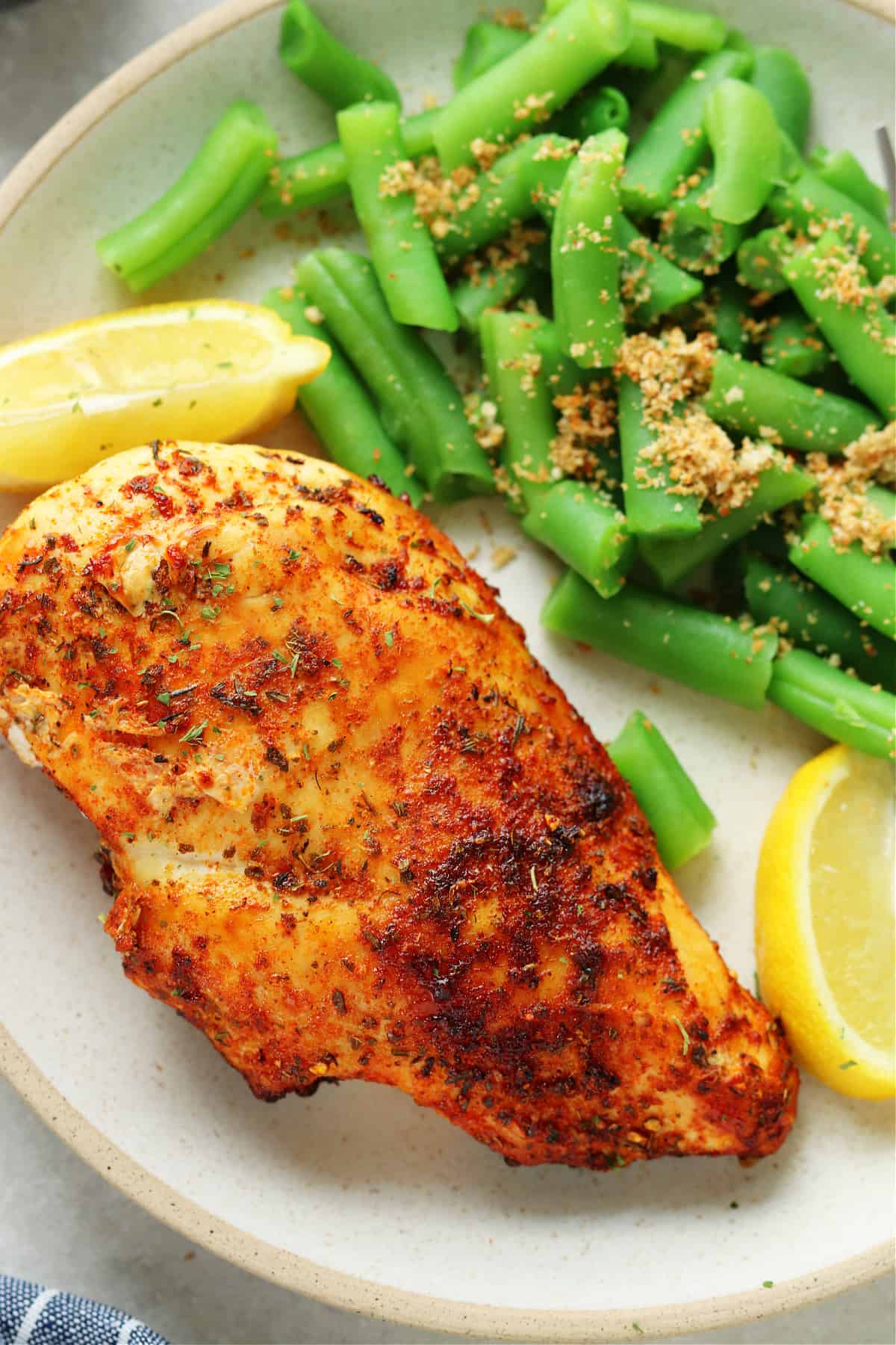 Air fried chicken breast with lemon wedges and green beans on a dinner plate with fork.