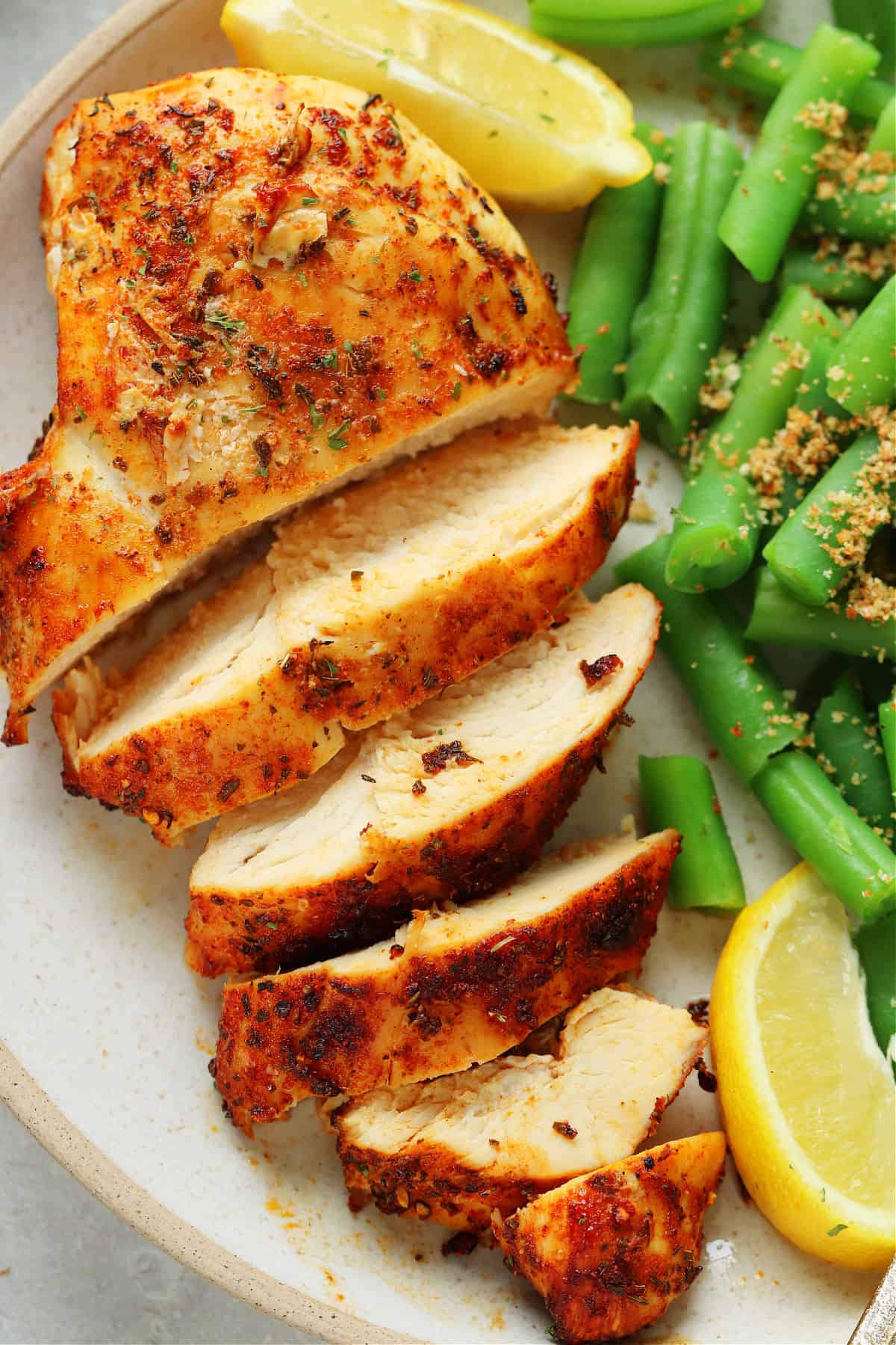 Sliced air fried chicken breast with green beans on the side, on a dinner plate.