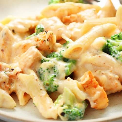 Square image of pasta with chicken and broccoli on a cream plate.