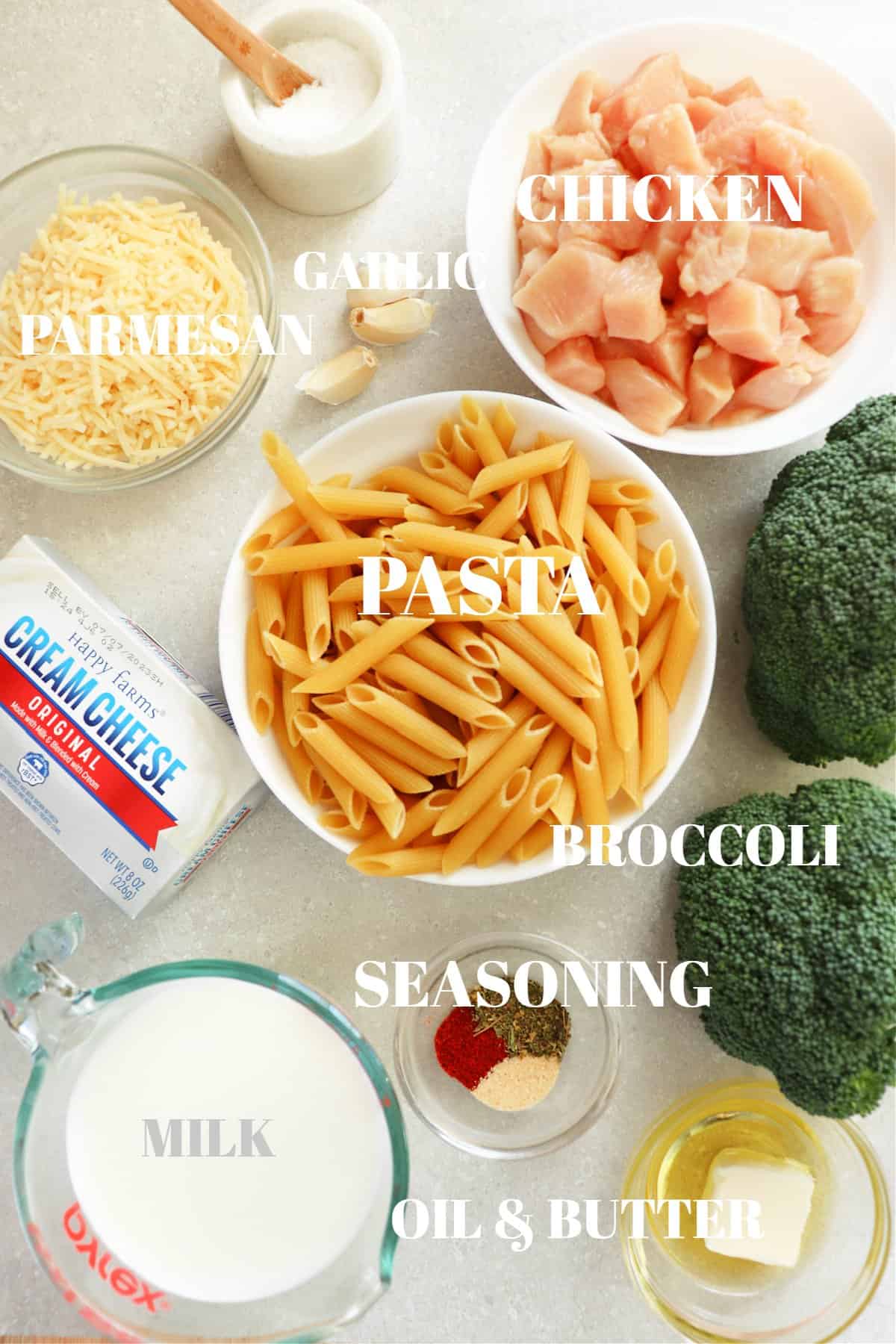 All ingredients for chicken and broccoli pasta on a gray board.