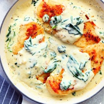 Three chicken breasts in a creamy sauce with spinach, in an enameled Le Creuset skillet.
