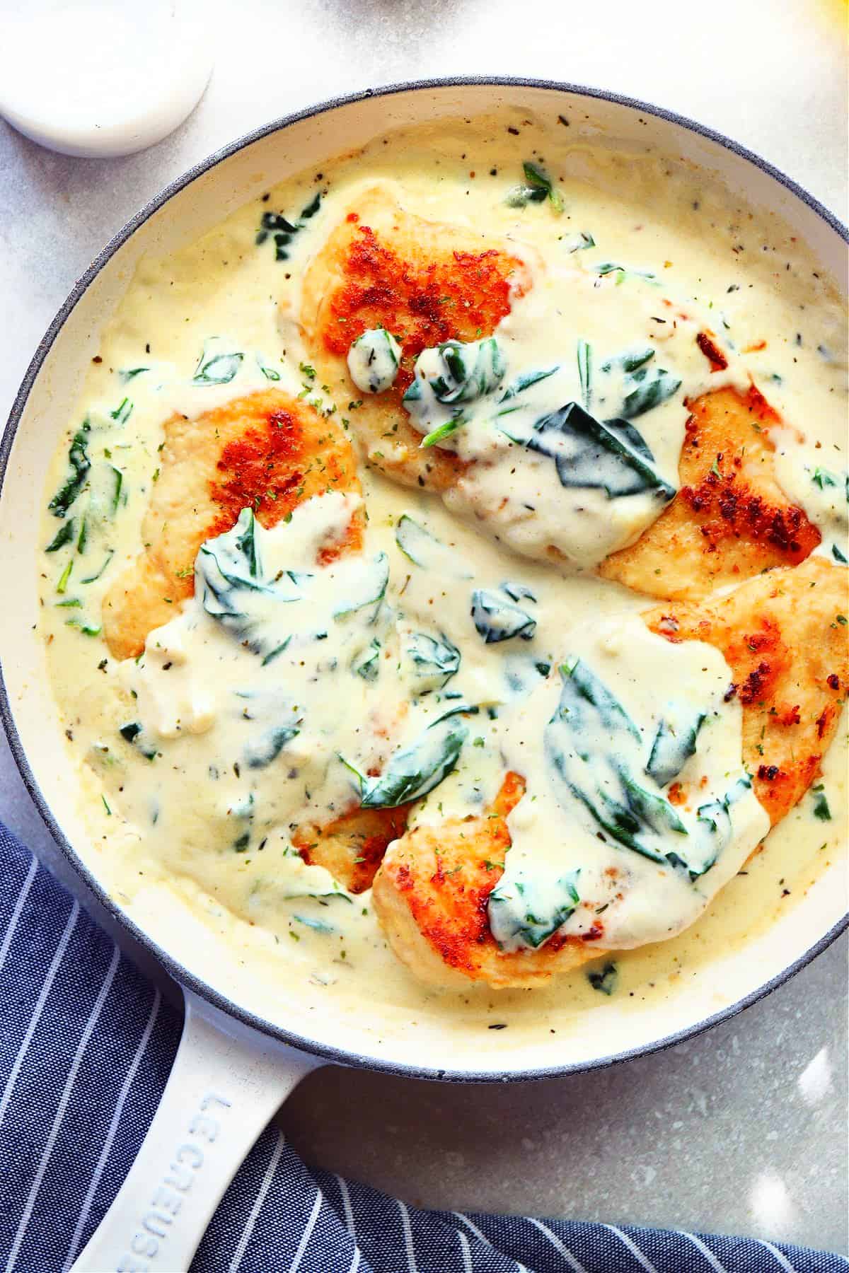 Three chicken breasts in a creamy sauce with spinach, in an enameled Le Creuset skillet.