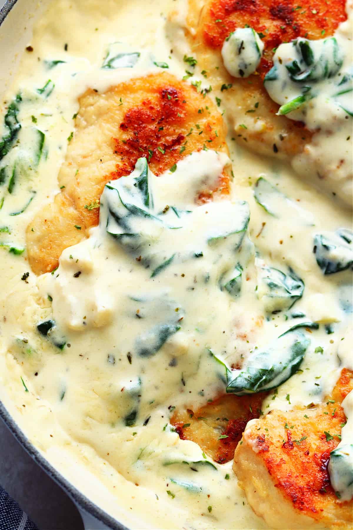 Cooked chicken breast in a creamy sauce with spinach in a pan.