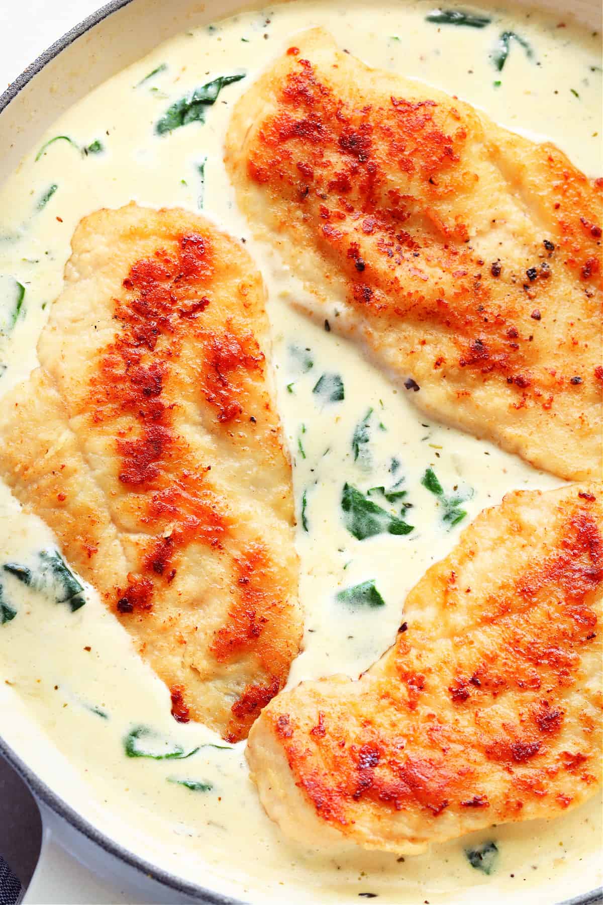 Three browned chicken breasts in a creamy spinach sauce in a white pan.