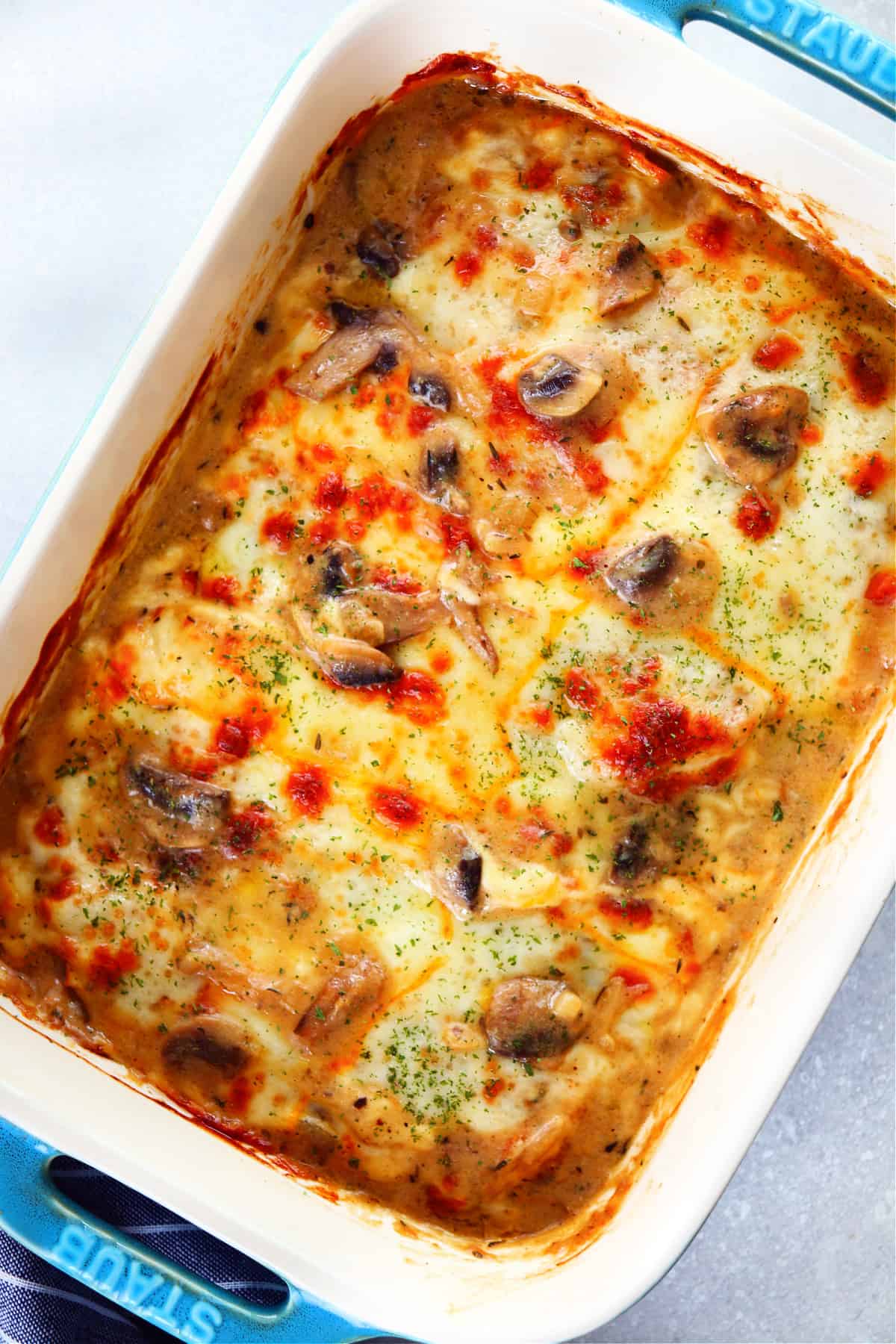 Chicken casserole with mushroom sauce and melted cheese in a blue Staub baking dish.