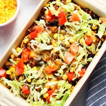 Casserole with taco meat, fresh tomatoes and lettuce in a rectangular baking dish.