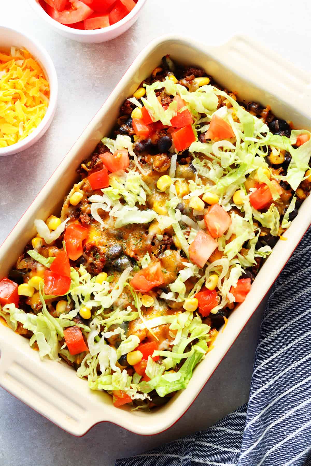 Casserole with taco meat, fresh tomatoes and lettuce in a rectangular baking dish.