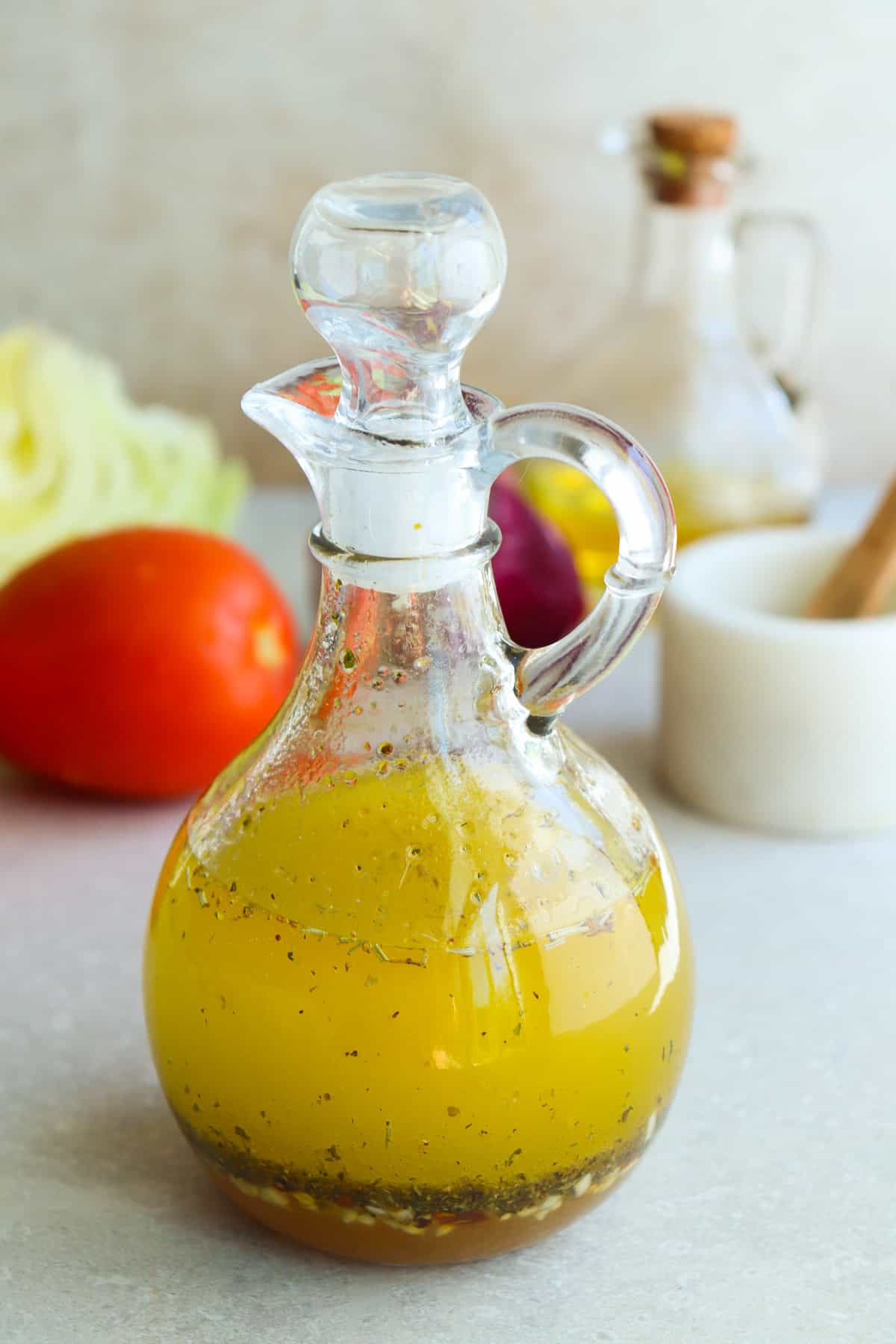 Italian dressing in a glass cruet on a gray board with Roma tomatoes behind it.