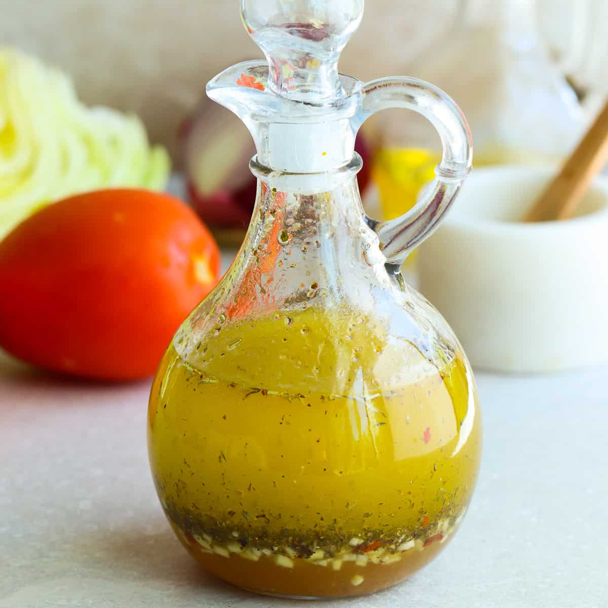 Square image of Italian dressing made from scratch, in a glass cruet with stopper on a gray board.
