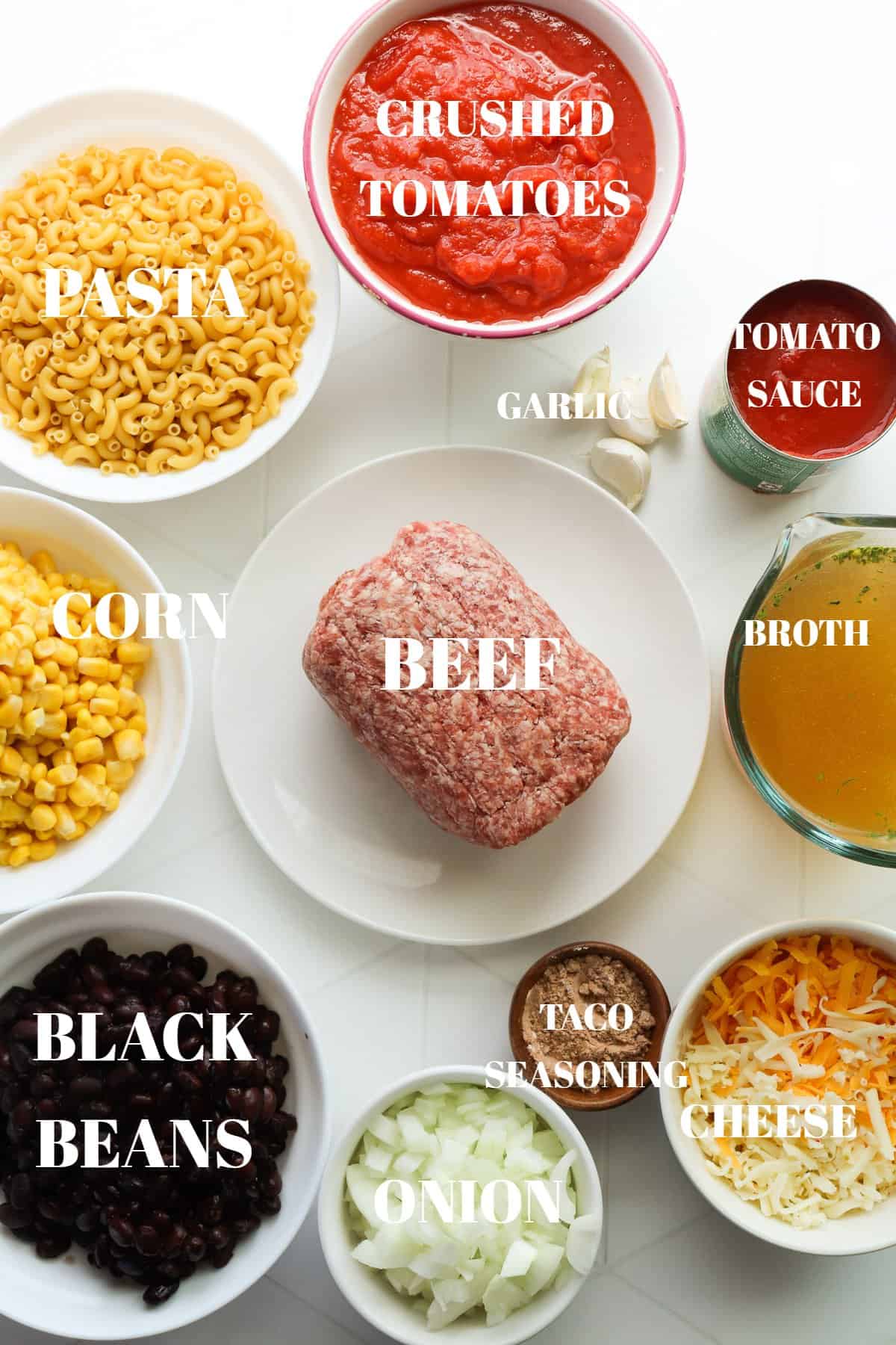 All ingredients for taco pasta in bowls on a white tile board.