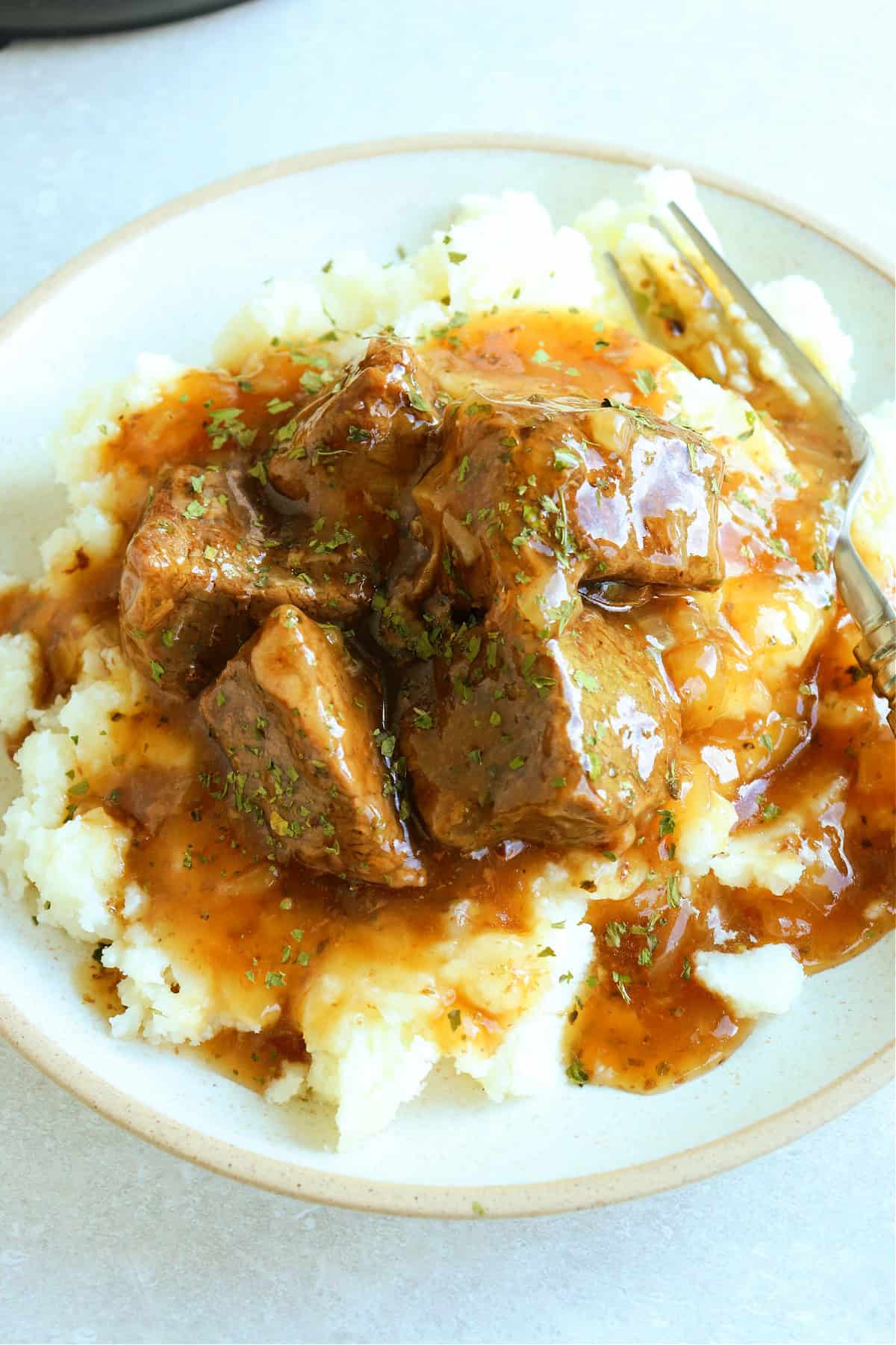 Overhead photo of beef tips in gravy on mashed potatoes, on a plate.