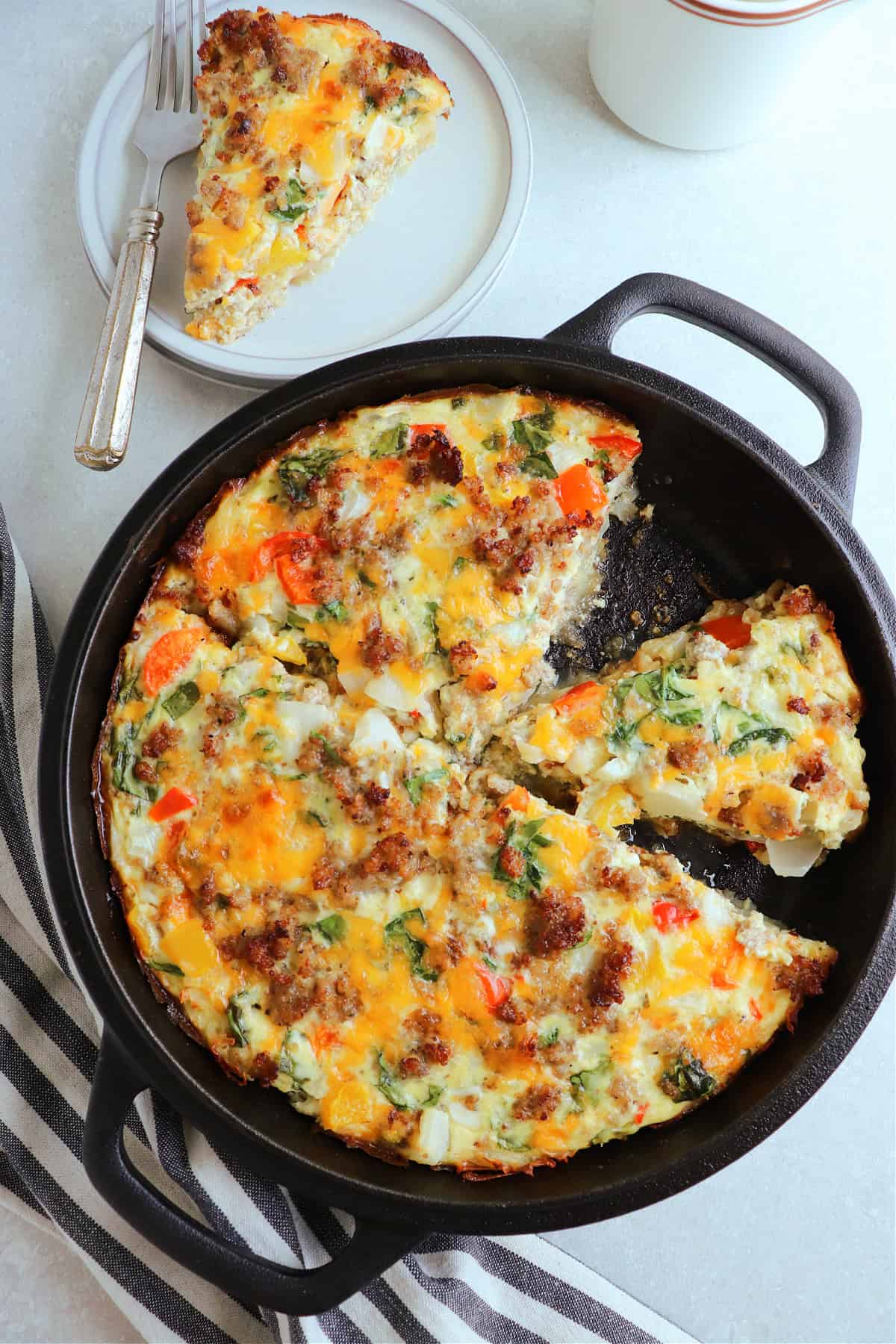 Above photo of crustless quiche in a cast iron skillet, with one slice on a plate in the upper left corner.
