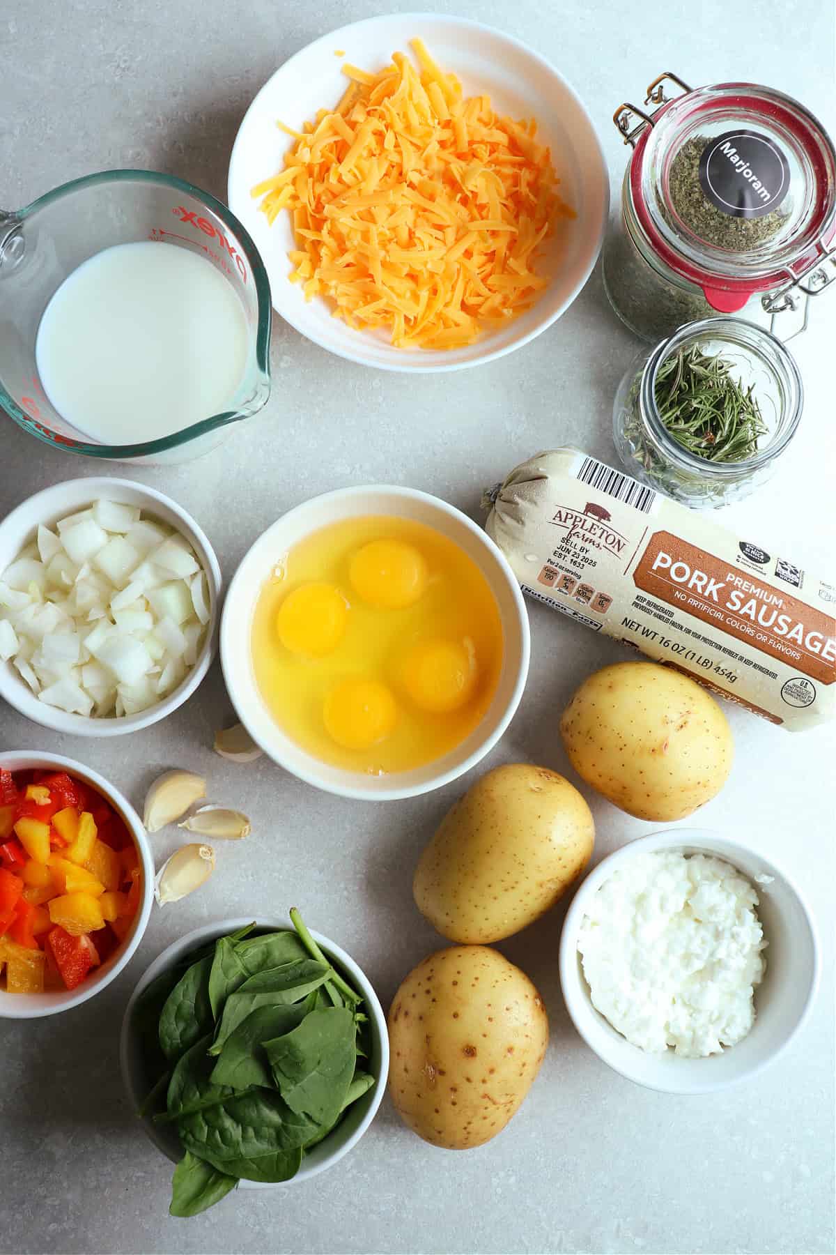 A photo of ingredients needed to make a quich with potato crust and ground sausage in the filling. All ingrdients are on a gray board, some in bowls.