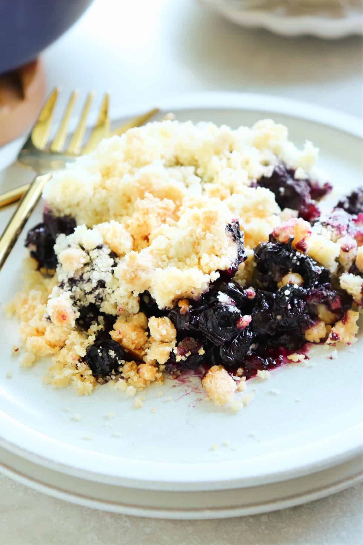 Close up shot of blueberry crumble on a small gray plate with gold forks on the left side.