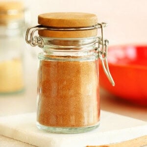 Square image of pumpkin pie spice in a small spice jar with clamp lid, set on a marble coaster.