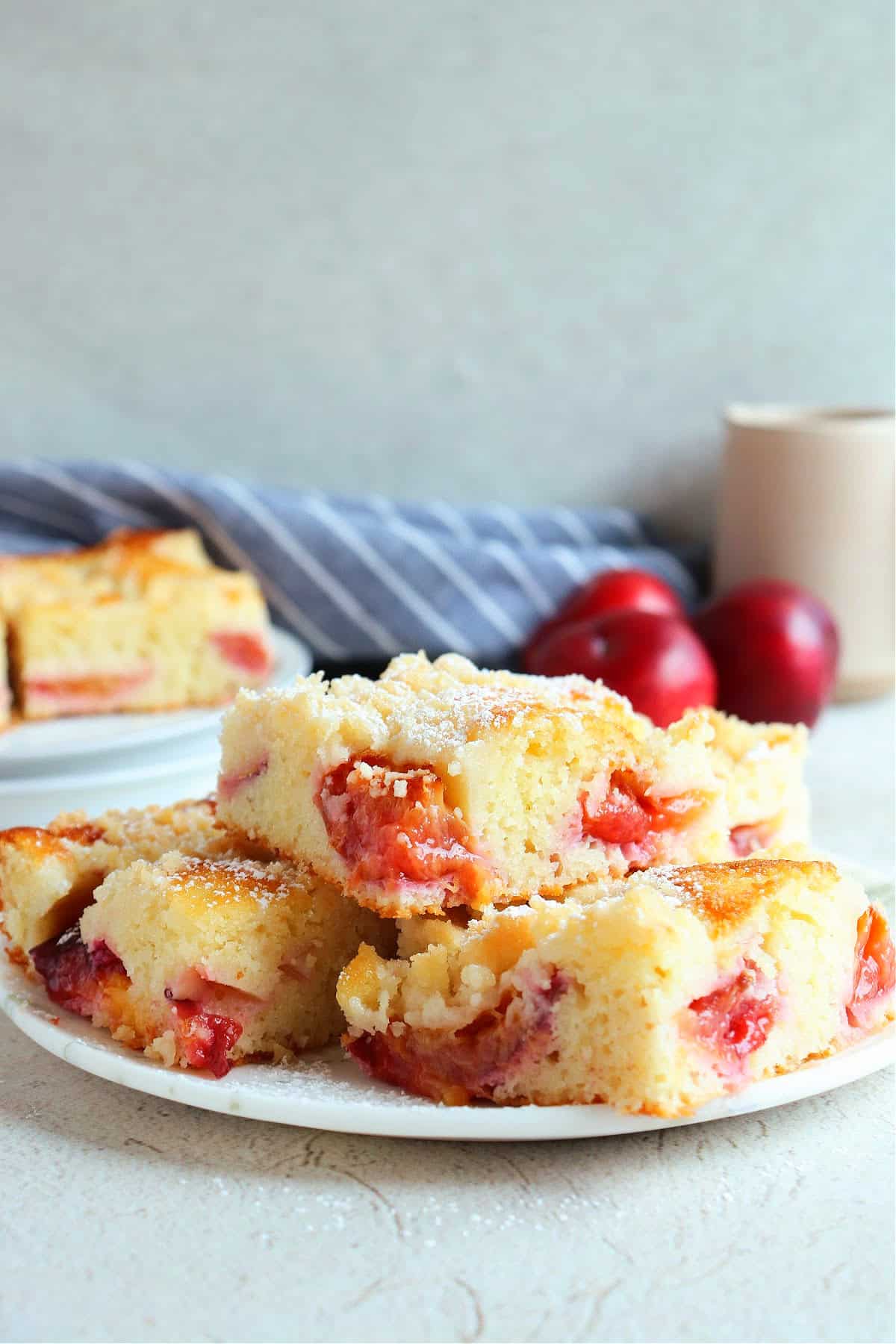 Three pieces of plum cake on a dessert plate, with fresh plums in the background.
